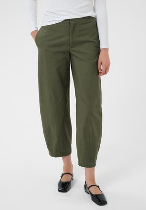 Personne portant un pantalon large court vert olive, un haut blanc à manches longues et des chaussures Mary Jane noires avec une bride et un talon bas.