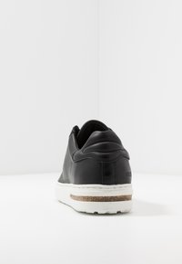 Baskets en cuir noir avec une finition lisse, un col rembourré et une semelle en caoutchouc blanc avec un accent en liège texturé.
