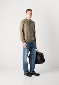 Kaki langermet polo med knappekrage, kombinert med lyseblå jeans. Modellen bærer en svart lærveske og har på seg svarte loafers.