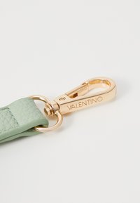 Světl zelený texturovaný kožený pásek se zlatou kovovou sponou. Spona na své straně nese vygravírovaný text "VALENTINO".