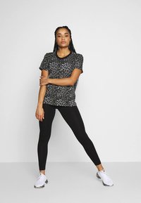 T-skjorte med korte ermer i svart og grå leopardmønster, kombinert med svarte leggings og hvite joggesko med mønstrede såler.