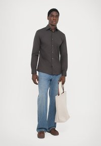Mørk knappet skjorte, lyseblå vide jeans, brune sko og en beige totebag med håndtak. Enkelt design, glatte teksturer.