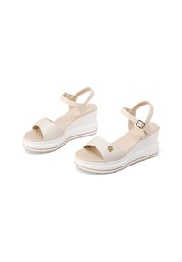 Sandali con zeppa in materiale sintetico color crema, con punta aperta, cinturino alla caviglia e logo decorativo. Presentano una suola piatta bianca con leggera texture.