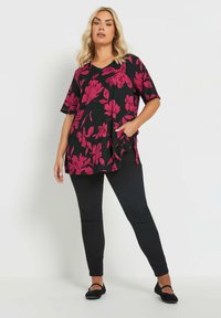 Túnica negra con flores magentas, mangas cortas, escote en V, bolsillos laterales, combinada con pantalones slim-fit negros y bailarinas negras.