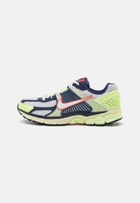 Ténis desportivos com parte superior em malha nas cores azul marinho, branco e amarelo neon, com um swoosh vermelho em contraste, sola almofadada e detalhes texturizados.