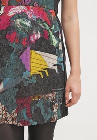 Barevný textil s abstraktními květinovými a geometrickými vzory v modré, růžové a žluté barvě. Černé akcenty po stranách a na lemu.