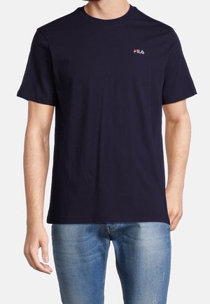 Homme portant un t-shirt FILA bleu marine foncé uni à manches courtes et un jean en denim bleu clair sur fond blanc.