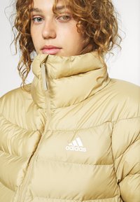 Beidzis pūkainais mētis ar augstu apkakli, kokvilnas dizainu un baltu adidas logo uz krūtīm. Gluda, spīdīga tekstūra ar rāvējslēdzēju.