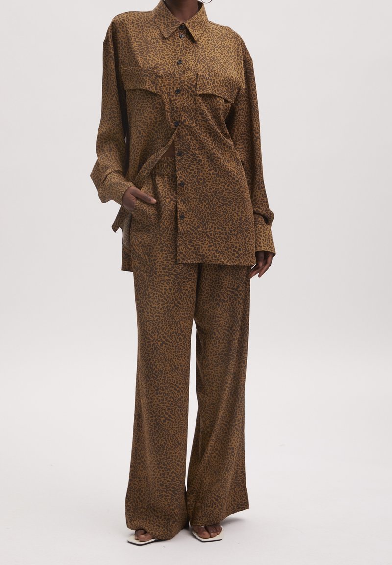 Chemise marron ample à imprimé léopard avec boutons, associée à un pantalon large assorti et des sandales à bout carré.