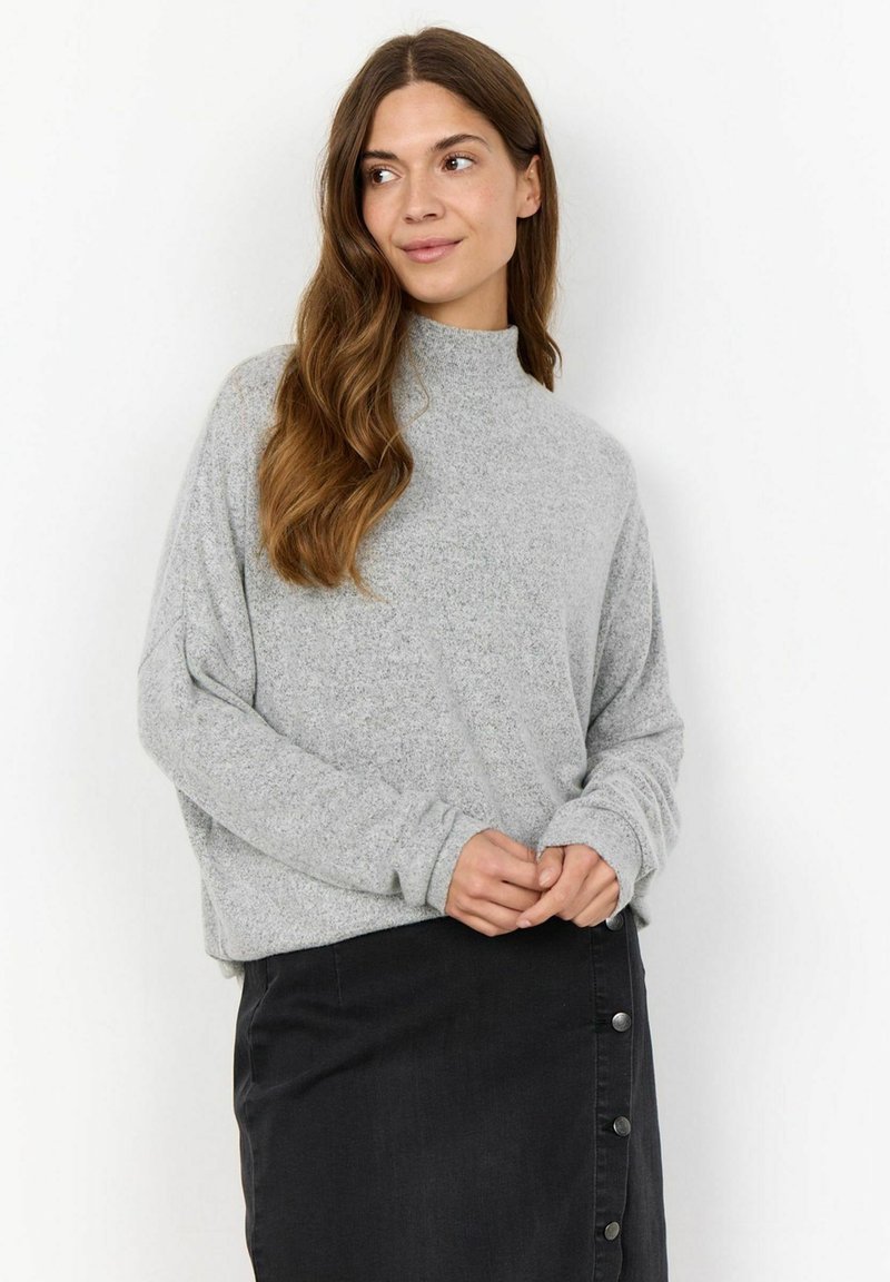 Grey, textured sweater with a high neckline and loose fit, paired with a black, knee-length skirt featuring button details on one side.