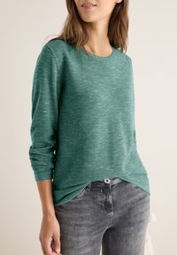Grün gestreifter Langarmpullover mit Rundhalsausschnitt, mit umgeschlagenen Ärmeln und lockerer Passform, kombiniert mit grauen Jeans.