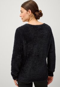 Zwarte, pluizige trui met een losse pasvorm, wijde halslijn en lange mouwen. De textuur lijkt zacht en comfortabel.