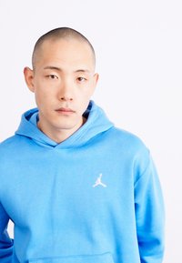 Sweatshirt à capuche bleu clair avec une texture douce et une poche kangourou. Présente un logo Jordan blanc sur la partie gauche de la poitrine.