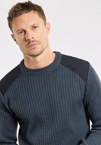 Dunkelblauer gerippter Pullover mit rundem Halsausschnitt und schwarzen Schulterakzenten. Die Textur ist gestrickt und weist ein figurnahes Design auf.