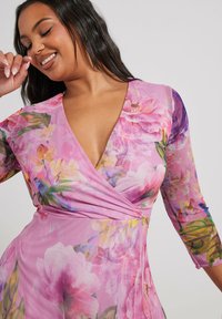 Vaaleanpunainen kukkakuvioinen kietaisumekko 3/4-hihasilla. Mekossa on V-aukko ja eloisat moniväriset kukkakuviot. Kevyt, teksturoitu kangas.