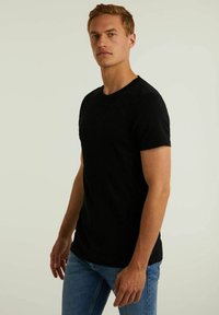 Fekete, rövid ujjú póló, kerek nyakkivágással, puha anyagból készült. A szabása slim fit, kék farmernadrággal egészül ki.