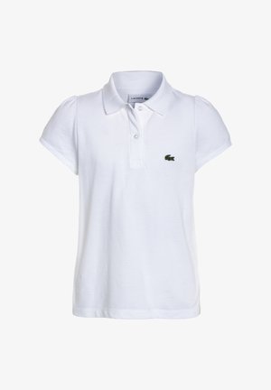 Biała koszulka polo z krótkim rękawem i zielonym logo, plisowana biała spódnica, różowa torebka i zielone skarpetki w paski. Całość uzupełniają casualowe trampki.