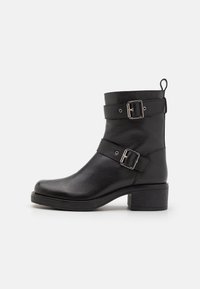 Black leather ankle boot with two adjustable straps, silver buckles, rounded toe, and a low stacked heel. Textured surface with sturdy outsole.