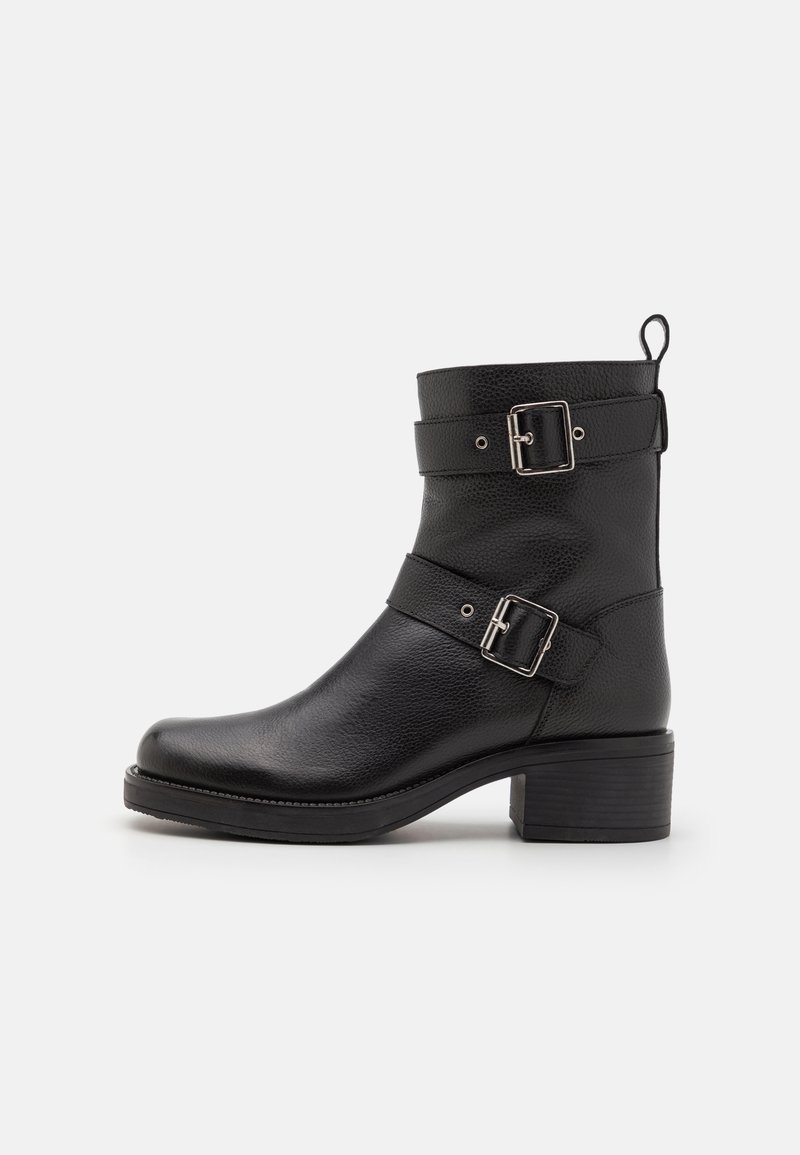 Black leather ankle boot with two adjustable straps, silver buckles, rounded toe, and a low stacked heel. Textured surface with sturdy outsole.