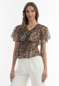 Brun, slangeprint bluse med V-hals, dobbel flæseærmer, elastisk talje og let, gennemsigtig stof, parret med hvide bukser.