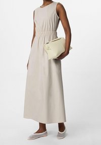 Robe maxi sans manches beige avec taille froncée, associée à un sac à main crème et des chaussures à enfiler tressées. Texture lisse, design minimaliste.
