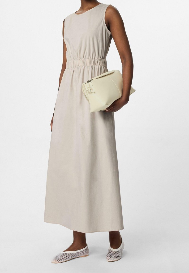 Robe maxi sans manches beige avec taille froncée, associée à un sac à main crème et des chaussures à enfiler tressées. Texture lisse, design minimaliste.