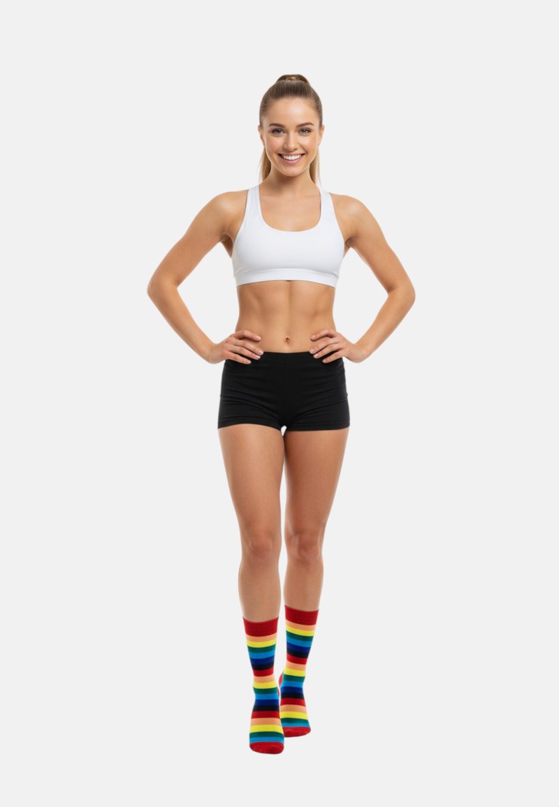 Modelo vistiendo un sujetador deportivo blanco y pantalones cortos negros, con calcetas de rayas coloridas en rojo, azul, amarillo y verde.