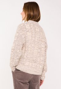 Maglione lavorato a maglia spesso in beige con motivo strutturato, scollatura rotonda e orlo a costine. La composizione in misto lana offre calore e morbidezza.