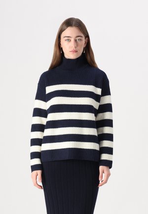 Pull à col roulé rayé bleu marine et crème avec une texture côtelée et une coupe décontractée. Manches longues avec détails au niveau des poignets, associé à une jupe côtelée assortie.