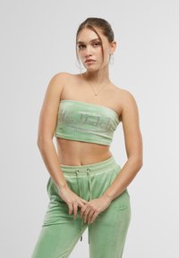 Zeleni baršunasti dvodijelni set koji uključuje bandeau top s logotipom od rhinestona i odgovarajuće trenirke svezane vezicom i vezom na detaljima.