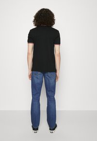 Polo shirt nera con dettagli del colletto in contrasto rosso e bianco, abbinata a jeans in denim blu. Fit classico e maniche corte.