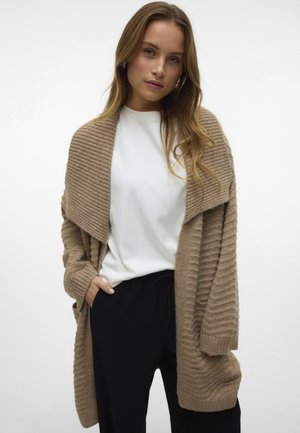 Beige ribbed cardigan with open front, long sleeves, and textured knit. Paired with a white top and black pants.