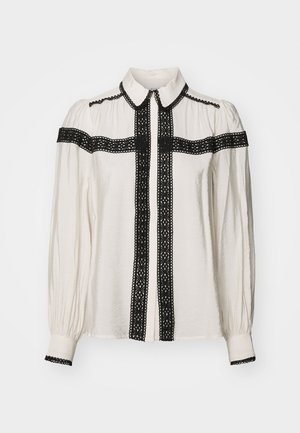 Balta blūze ar melnu mežģīņu dekoru priekšpusē, apkaklē un piedurknēs. Ir garas piedurknes un pogu aizdare.