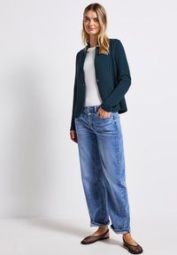 Mörk teal figurerad blazer, vit topp, ljusblå vida jeans och svarta meshballerinas. Blazern har en rund halsringning och knäppning.