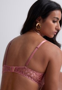 Soutien-gorge en dentelle et satin dans une teinte rose poussiéreux avec des bretelles réglables, du matériel décoratif et un motif texturé sur le tissu.