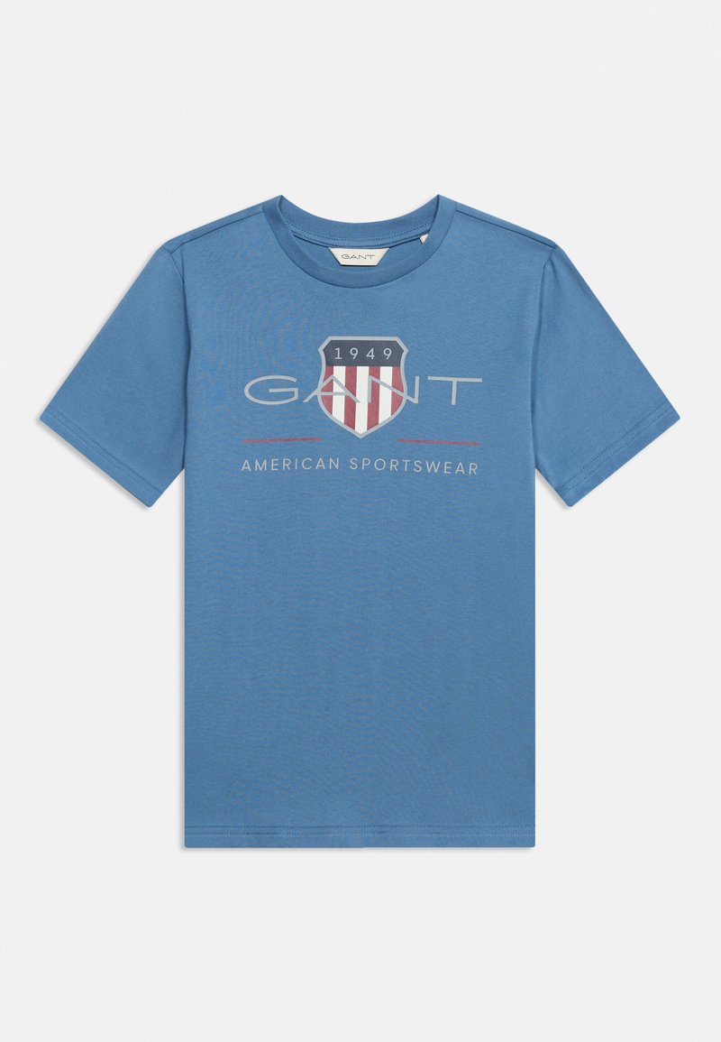 Μπλε κοντομάνικη μπλούζα με λογότυπο ασπίδας που αναγράφει "1949", τη λέξη "GANT" και "American Sportswear" τυπωμένα στο στήθος.
