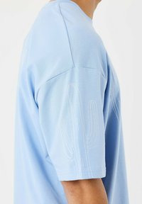 Camisa de algodón de color azul claro con mangas cortas, que presenta bordado de cactus blanco en la parte superior de la manga. Textura suave y corte relajado.