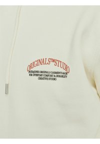 Krämfärgad hoodie i mjukt tyg, med en framficka och snörning i huvan. Framträdande text i röd och svart brodyr på bröstet.