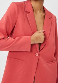 Blazer coral con solapa con muesca, cierre de un solo botón y dos bolsillos delanteros. Tejido suave y texturizado con corte entallado.