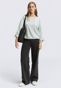 Light mint green blouse with gathered sleeves, paired with high-waisted black wide-leg pants. Model carries a black tote bag and wears white shoes.