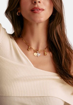 Gold chain necklace with various charms: a bell, a round tag with "BBB," a dove, and a small figurine. Textured links and shiny finish.