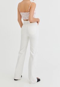 Hvide flared jeans med høj talje, lavet af bomulds materiale, baglommer og en elfenbensfarvet struktur, parret med en cropped, mønstret top.
