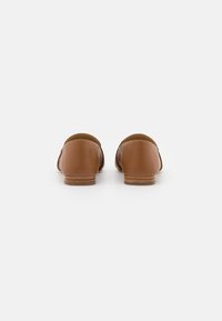 Scarpe in pelle marrone con tacco basso in legno. Parte posteriore arrotondata con una superficie liscia e senza chiusure visibili. Design semplice e minimalista.