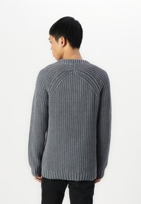 Grå stickad tröja med en texturerad, ribbad mönster, rund halsringning och sänkta axelsömmar, med en avslappnad passform och ribbade ärmslut.