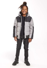 Pelēks un melns pufīgs mētelis ar kapuci, ar rāvējslēdzēja aizdari un sānu kabatām. Valkāts ar melnām džinsām un melniem sporta apaviem.