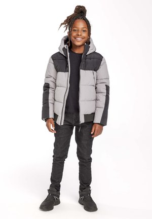 Padded jakna v sivo-črni barvi s kapuco, ki ima zadrgo in stranska žepa. Nosite jo s črnimi kavbojkami in črnimi supergami.