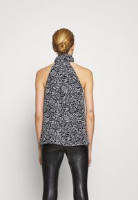 Top sin mangas de estampado floral en blanco y negro con un diseño en cascada, tela suave, con lazos en el cuello, acompañado de pantalones ajustados de cuero negro.