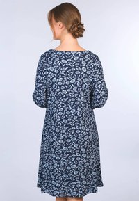 Dunkelblaues Kleid mit einem floralen Muster in Hellblau, mit rundem Ausschnitt und lockeren Ärmeln. Weicher, strukturiert Stoff.