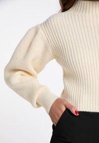 Tej ribbed pulóver magas gallérral, hosszú puff ujjakkal és testhez simuló derékkal. Puha, texturált kötött anyagból készült.