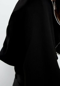 Černé ošacení s volnými rukávy jako capa a třpytivým stříbrným akcentem podél výstřihu, které má hladkou, texturovanou látku.